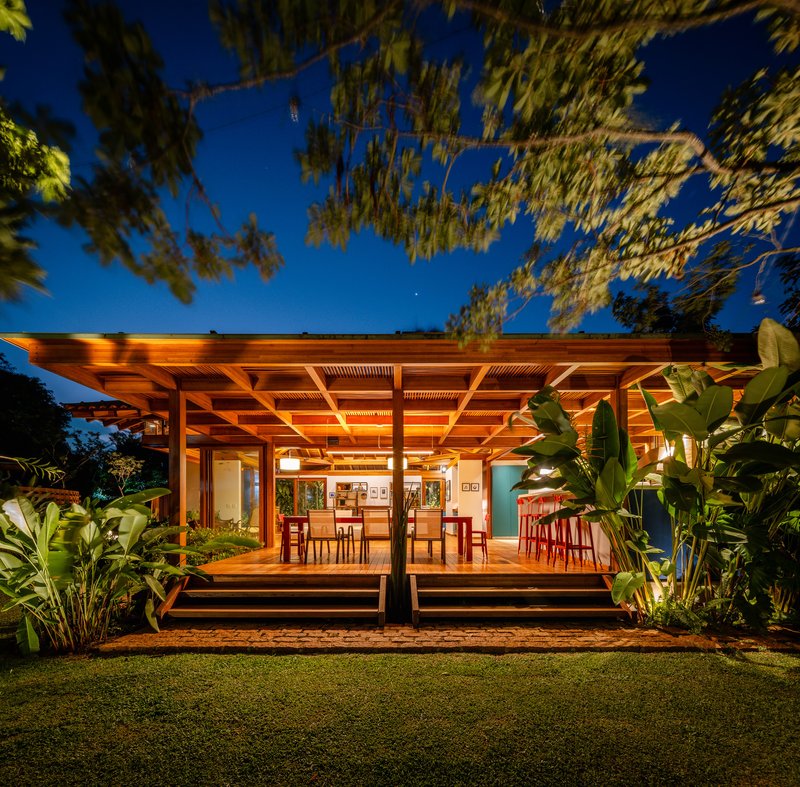 Flat timber pergola with slatted ceiling panels sheltering dining terrace and lawn at blue hour