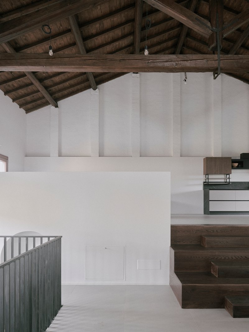 Interior view of dark timber staircase rising beneath exposed wooden roof trusses and white walls