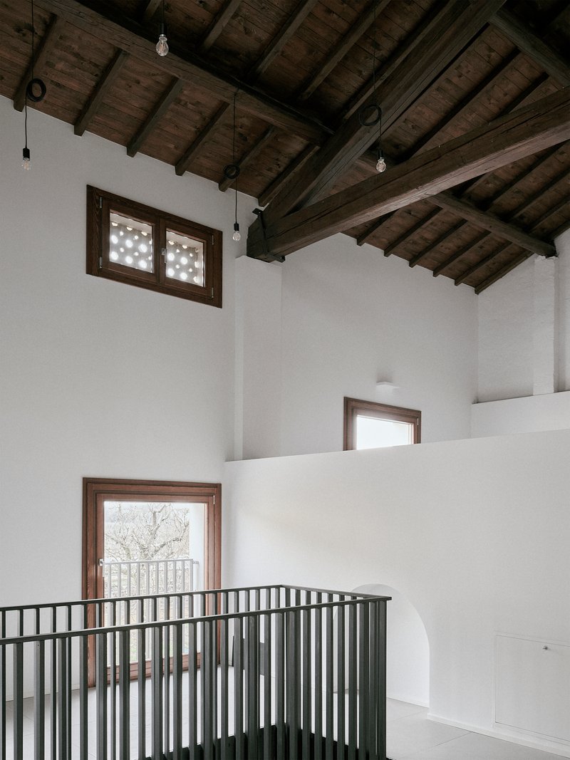 Double-height space with metal railing balcony and timber-framed windows overlooking bare winter trees