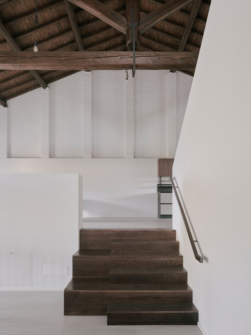 Dark oak staircase ascending toward white plaster walls beneath heavy timber roof trusses