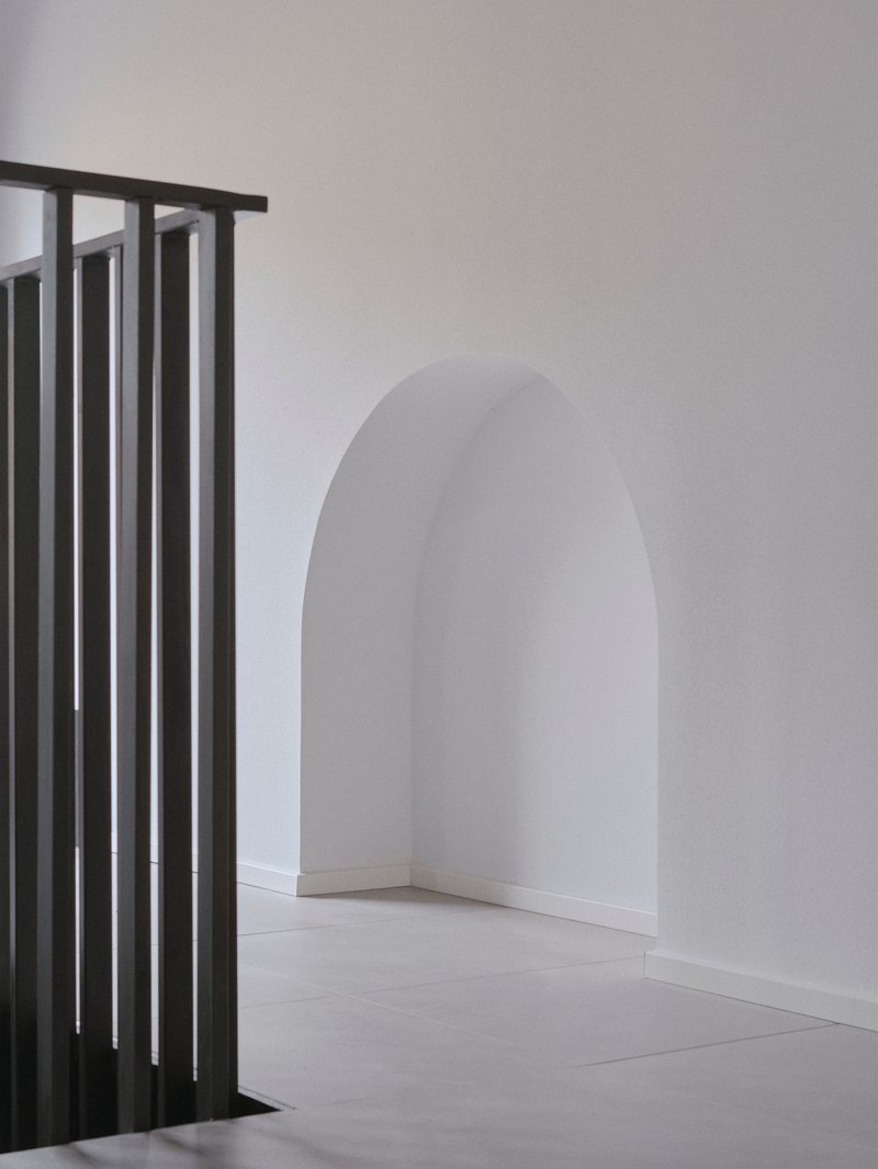 Metal slat balustrade beside an arched doorway with white plaster walls and pale flooring