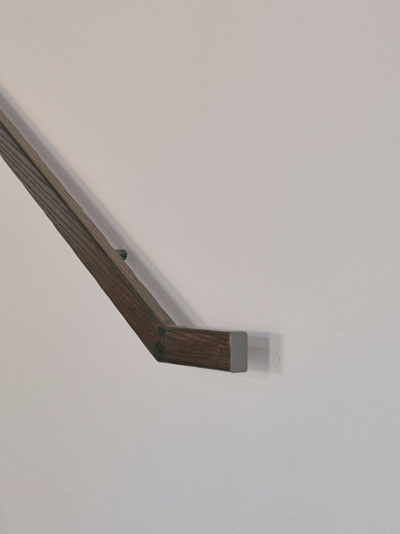 Close-up of a timber handrail with metal bracket mounting against a white wall