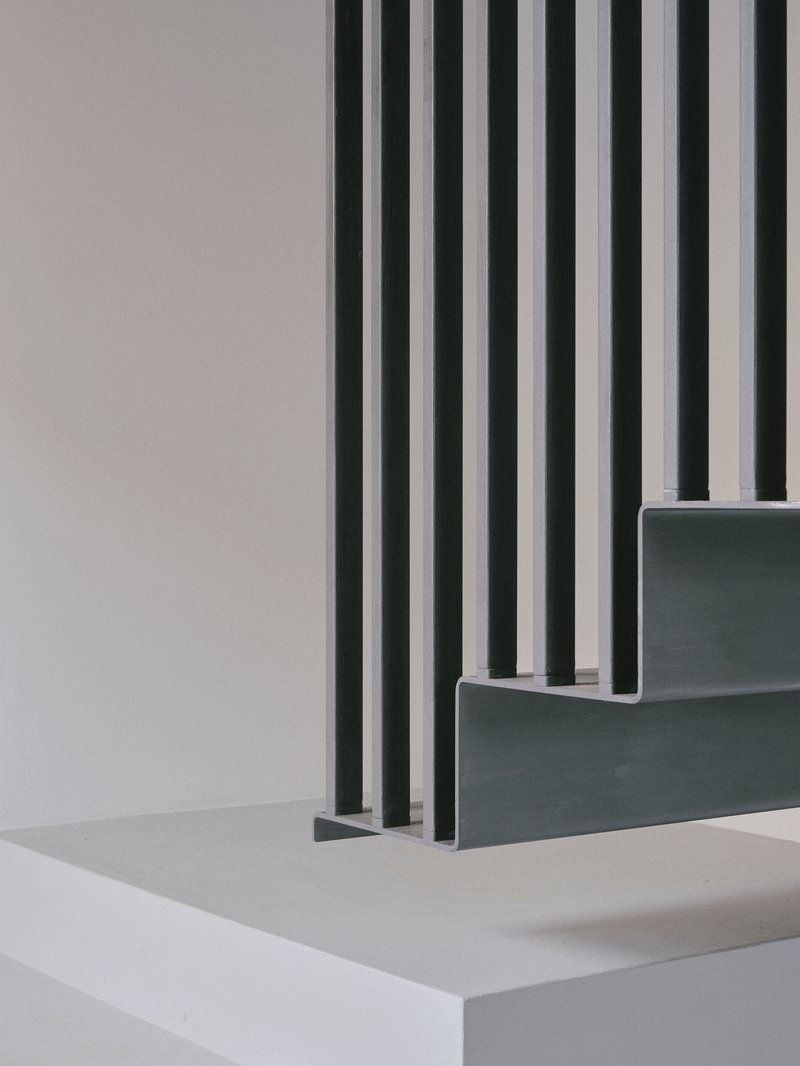 Detail of grey stairs with vertical metal rods passing through the treads and landing
