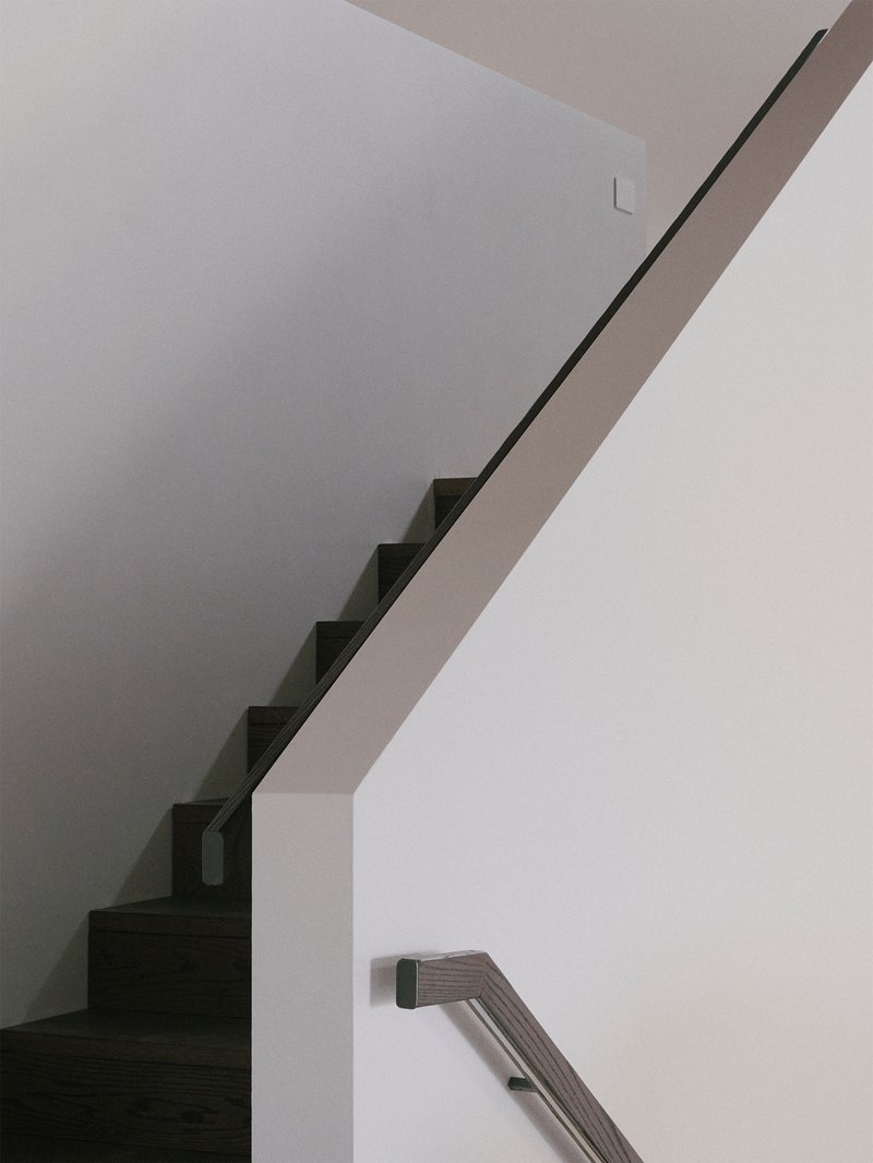 Interior view of cantilevered staircase with thin metal handrail ascending along white walls