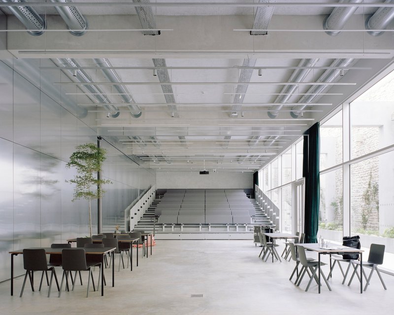 Retractable tiered seating emerging from the floor beneath a gridded ceiling with exposed mechanical systems