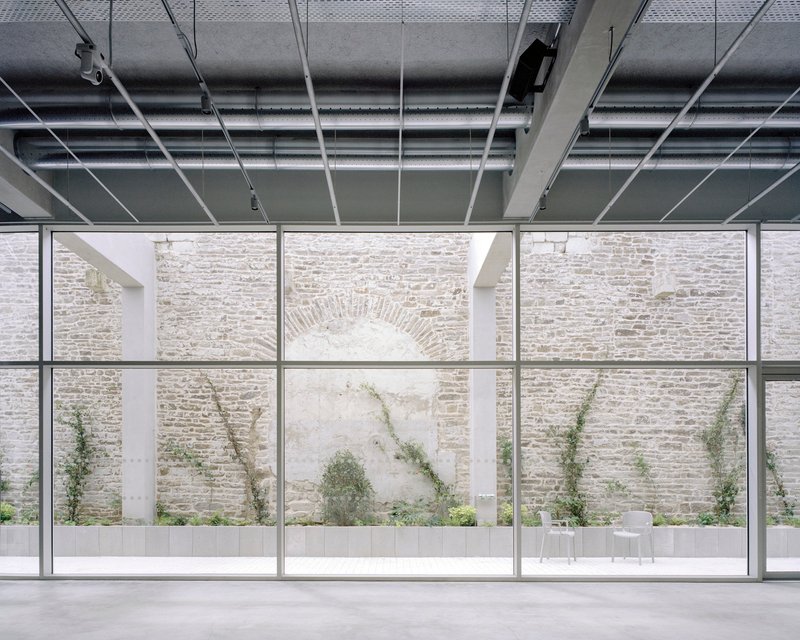 Floor-to-ceiling glazing framing a limestone courtyard wall with climbing vines and a bricked arch