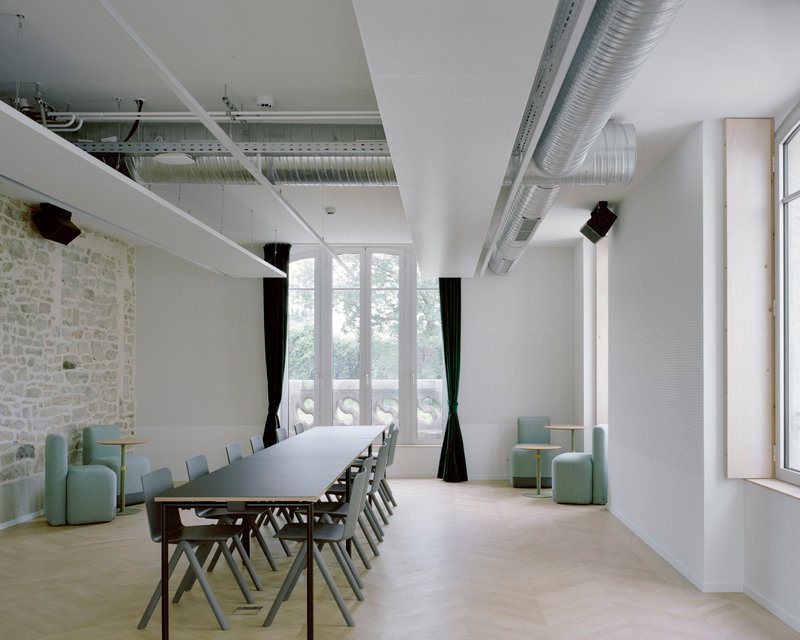 Meeting room with exposed stone wall, suspended ductwork, long white table, and green upholstered seating