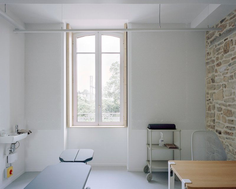 Interior workspace with perforated sliding panels flanking an arched window overlooking a courtyard with trees
