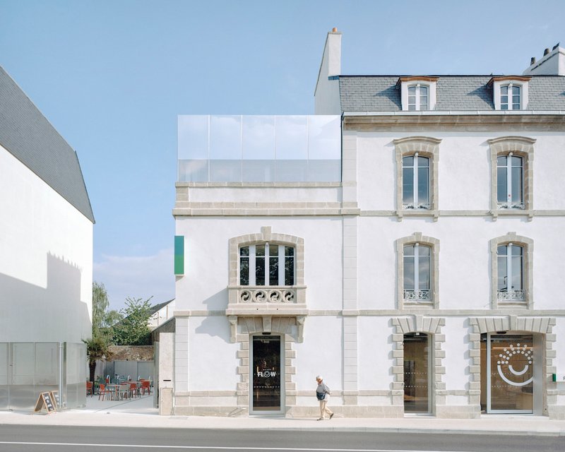 Street facade showing white-painted stone building with arched windows and translucent panel addition above