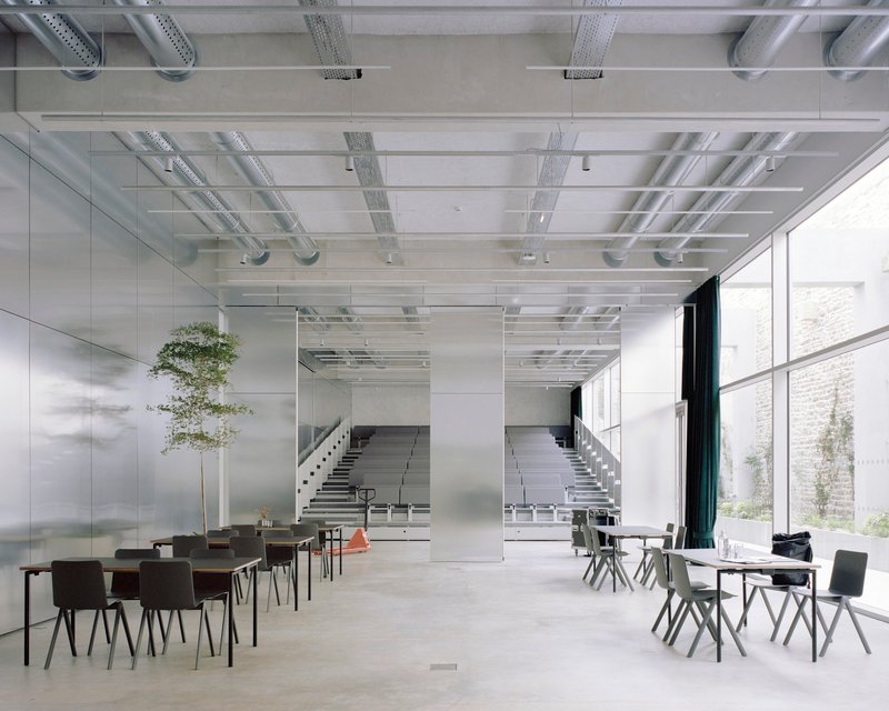 Interior foyer with exposed ceiling ducts, polished concrete floor, seating areas and twin staircases beyond