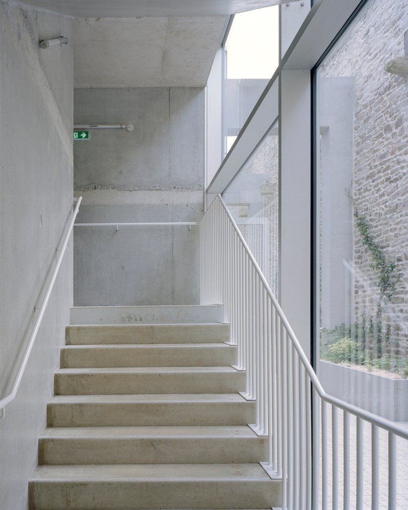 Concrete staircase with white metal balustrade and skylight above in diffused daylight