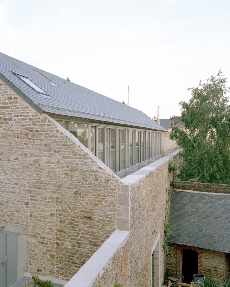 Stone courtyard walls with vertical glazing inserted beneath a slate roofline and adjacent tree