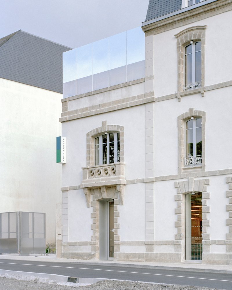 Street facade showing arched windows with stone trim and glazed box addition above under overcast sky