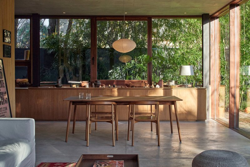 Open plan dining area with timber table and floor-to-ceiling glazing overlooking planted vegetation