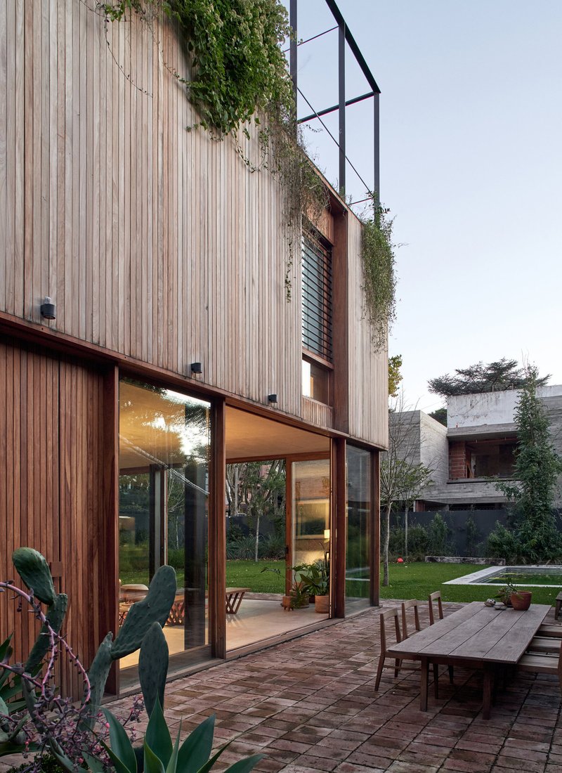 Vertical wood-slat facade with green roof plantings above full-height glazing and a terrace at dusk