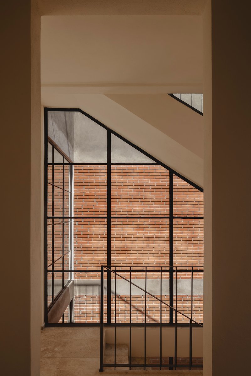 Black steel framed window casting diagonal shadows across white interior walls facing brick courtyard