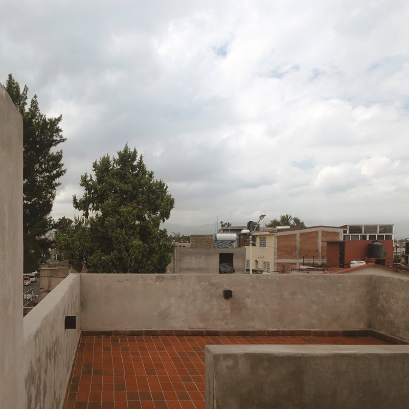 Rooftop terrace with red clay tile flooring and concrete parapet walls under overcast sky
