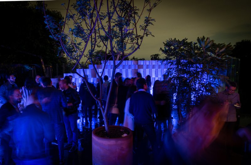 Event gathering in courtyard with visitors mingling among planted trees at night