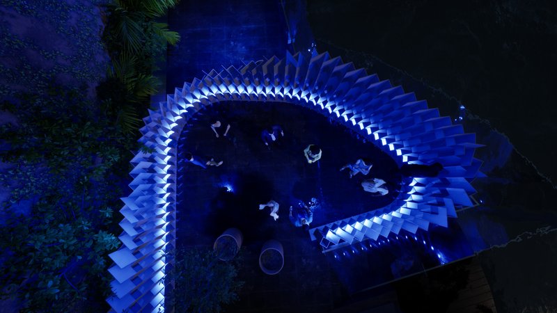 Overhead view of curved illuminated seating installation encircling visitors gathered at night beneath palm trees