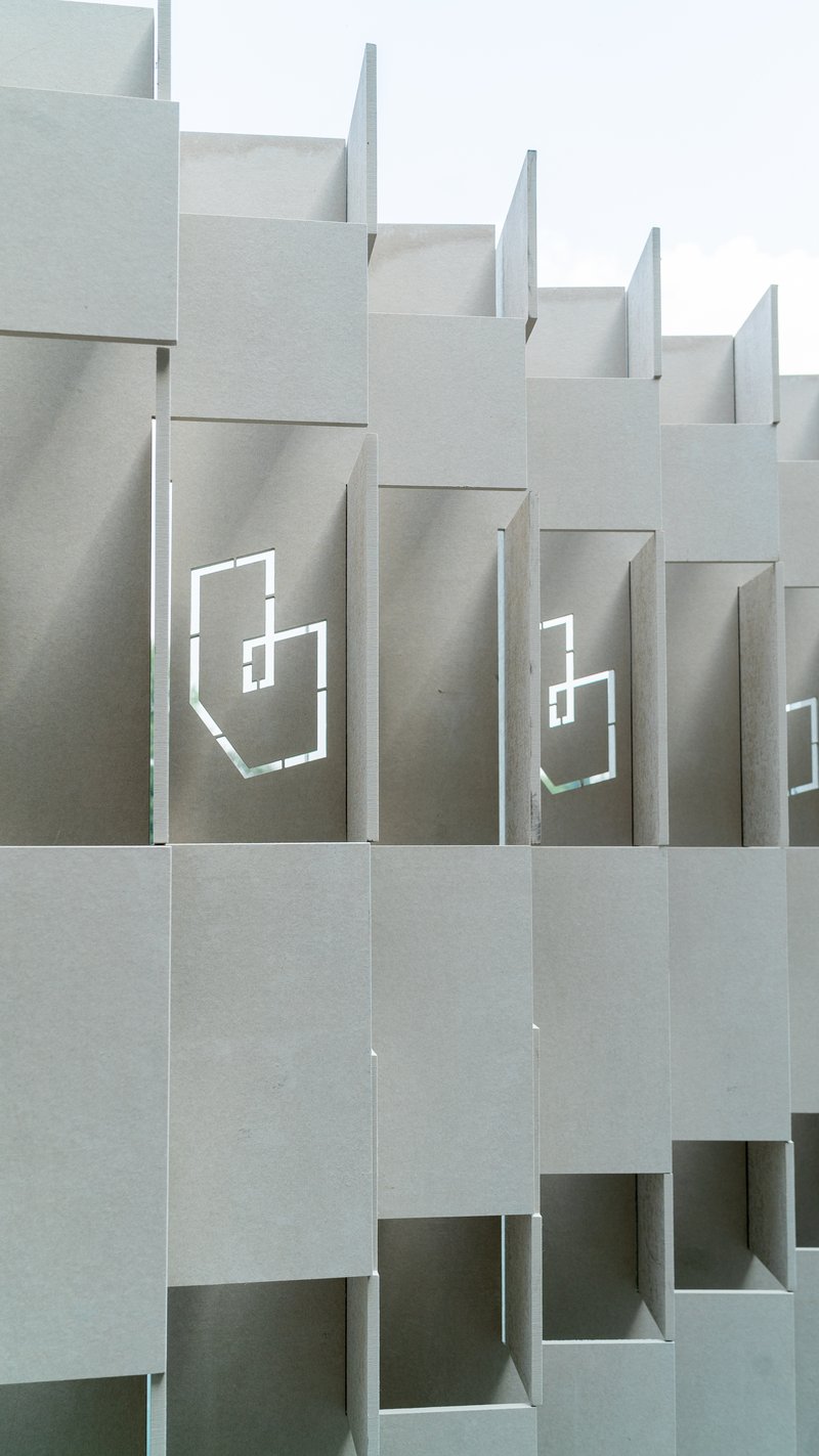 Stepped facade featuring staggered concrete volumes with recessed geometric logo cutouts under overcast sky