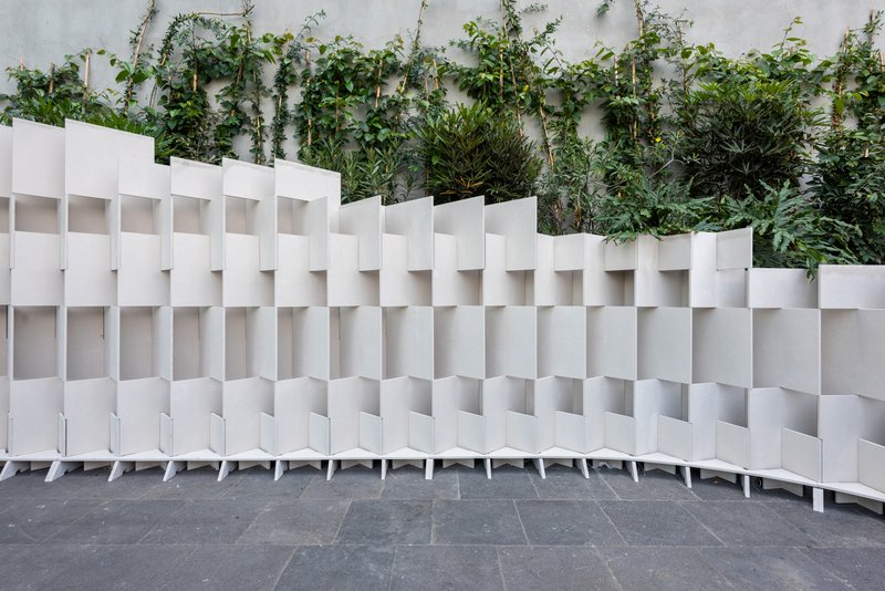 Curving white modular partition with alternating solid and void panels backed by wall-trained greenery