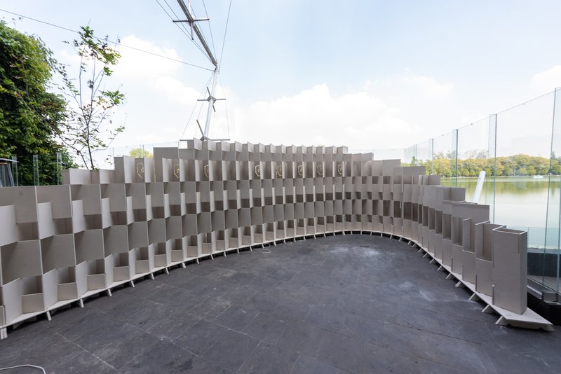 Curved grey modular seating wall with a pixelated surface pattern overlooking a pond with trees