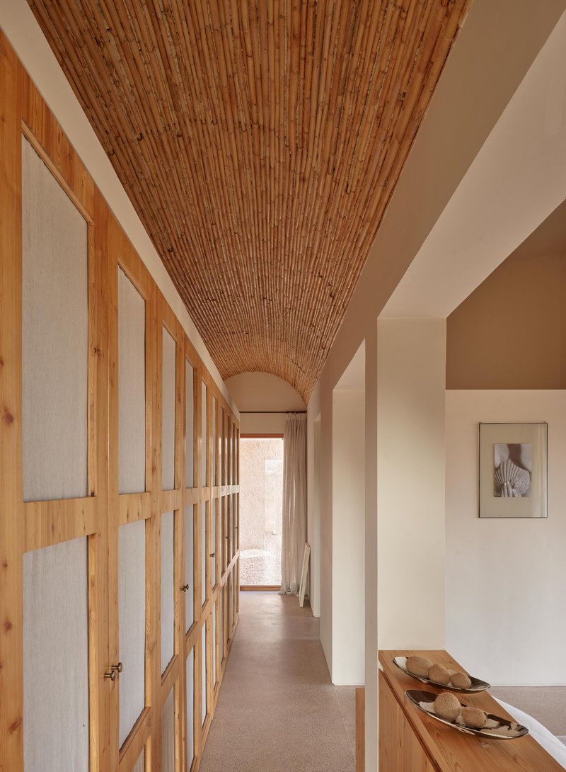 Hallway with continuous bamboo barrel vault ceiling, timber storage doors with frosted panels, and a framed artwork