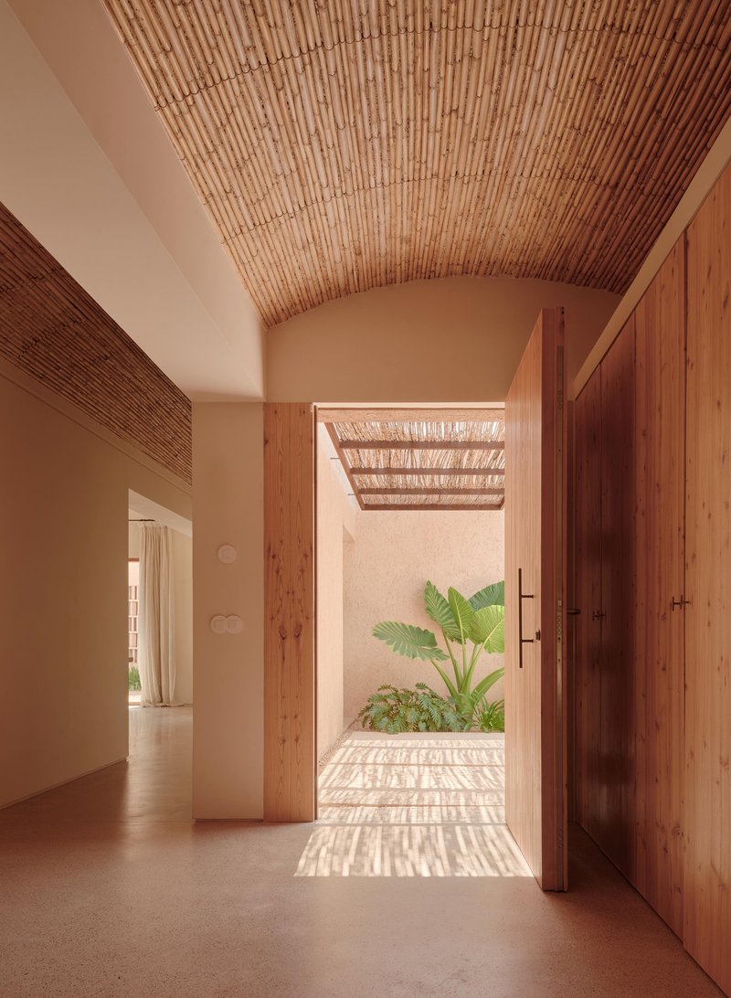 Interior hallway with vaulted slatted ceiling framing view to courtyard garden with dappled shadow