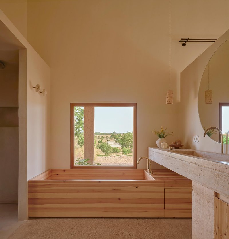 Timber-clad soaking tub positioned beneath a wide window overlooking the arid landscape beyond