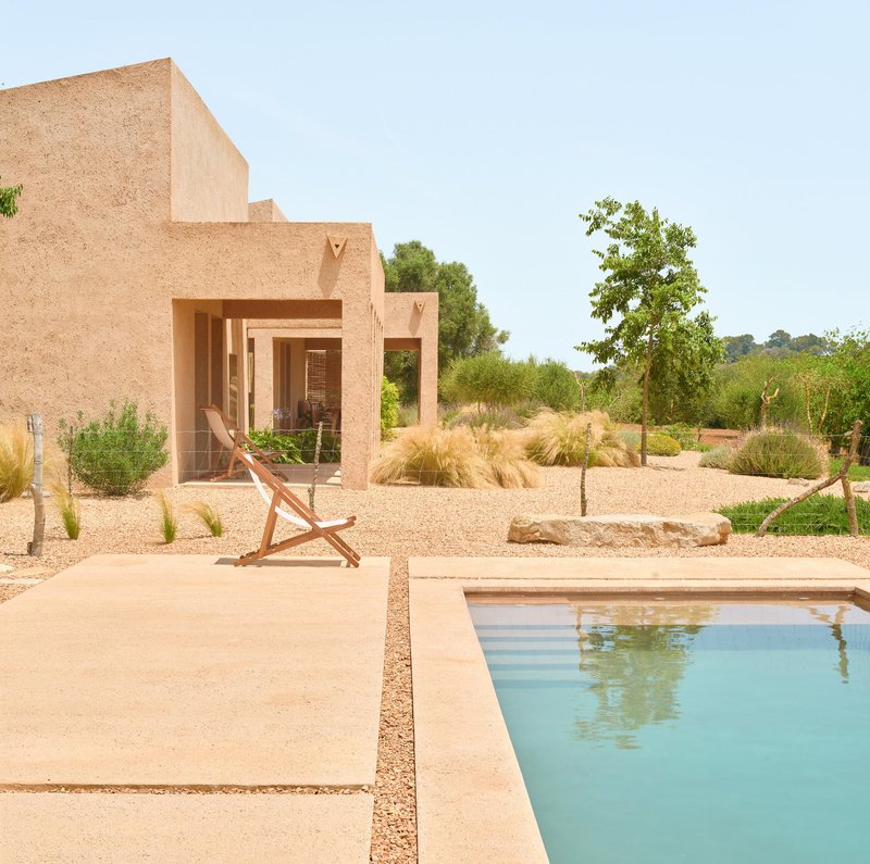 Swimming pool beside terrace with deck chair and straw-textured volumes overlooking gravel garden in daylight