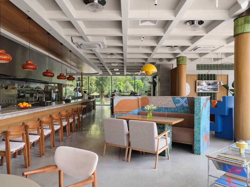 Open dining space with coffered white ceiling, cylindrical timber columns, and floor-to-ceiling glazing overlooking greenery