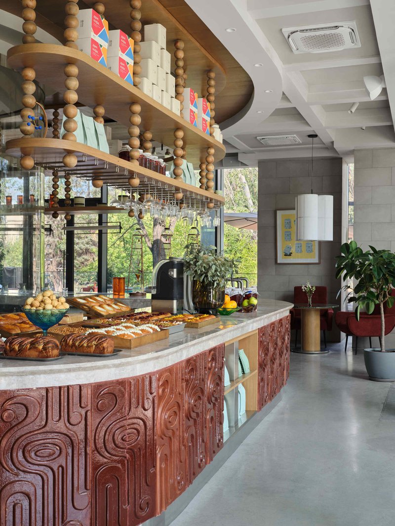 Curved bakery counter with carved timber cladding beneath a suspended shelf with wooden beads
