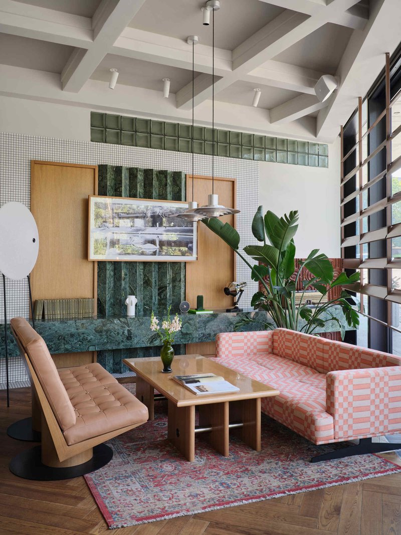 Lounge seating around green marble table with mosaic wall and timber cabinetry behind