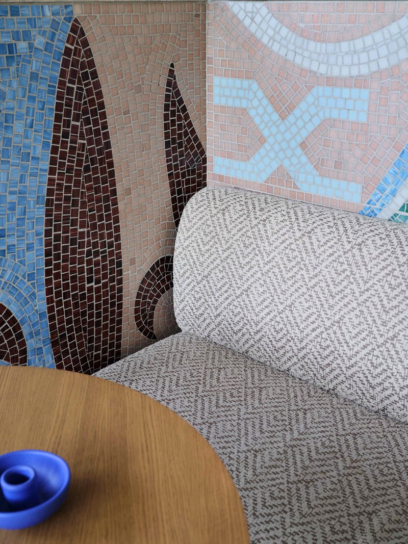 Corner seating with chevron upholstery against colorful mosaic wall featuring cypress tree motifs in blue and brown