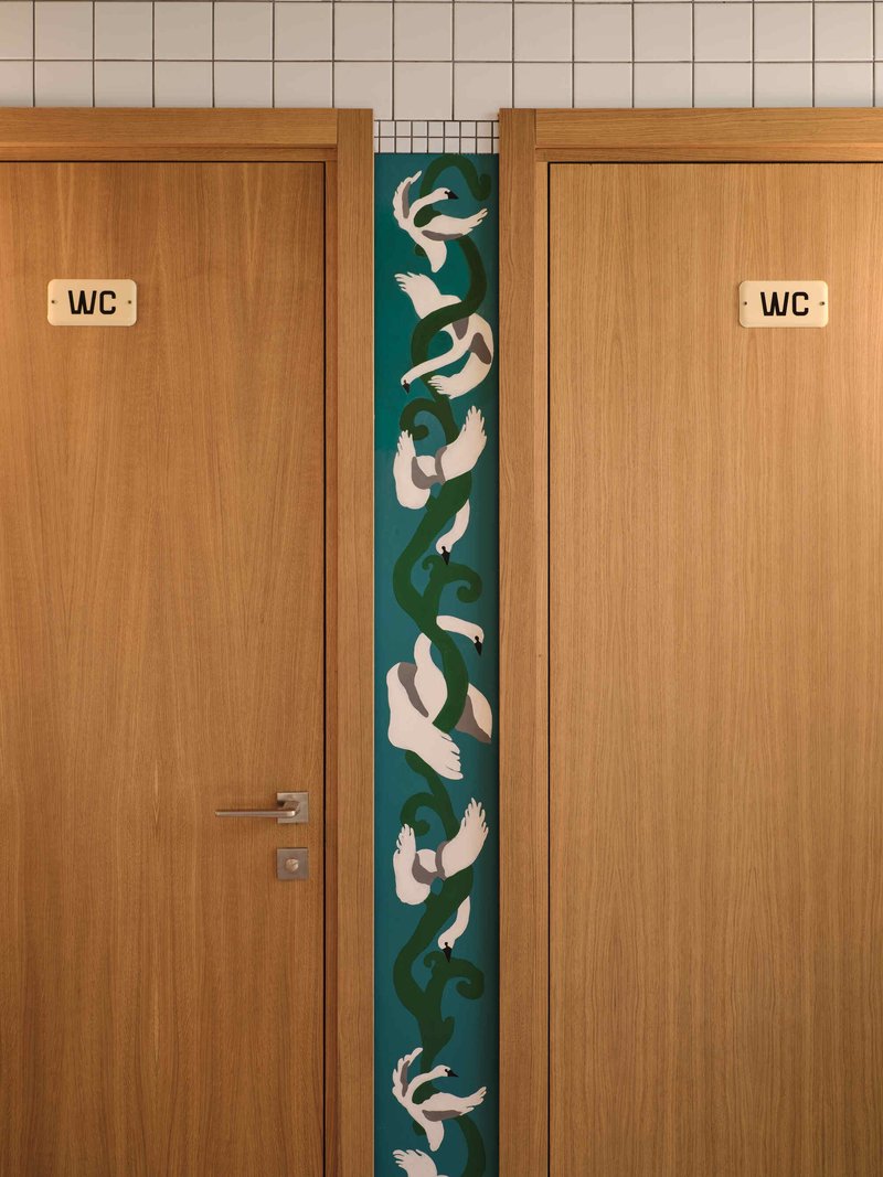Pair of oak restroom doors flanking a vertical tile panel with koi fish mosaic in blue and green