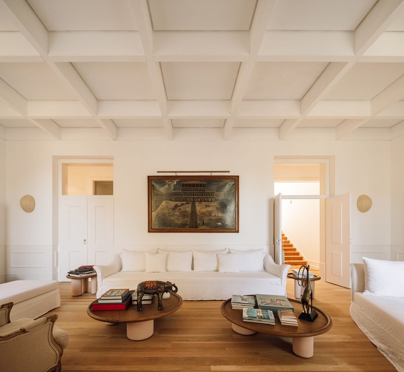 White coffered ceiling above a salon with timber floors and symmetrical doorways flanking a framed painting