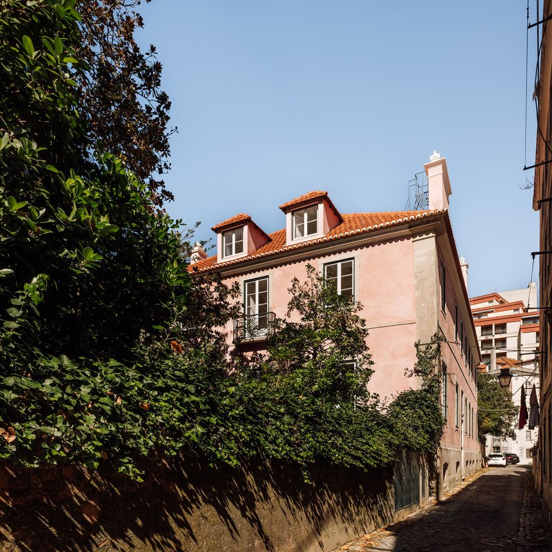 Pink rendered facade with terracotta roof dormers and wrought iron balcony viewed from a narrow lane
