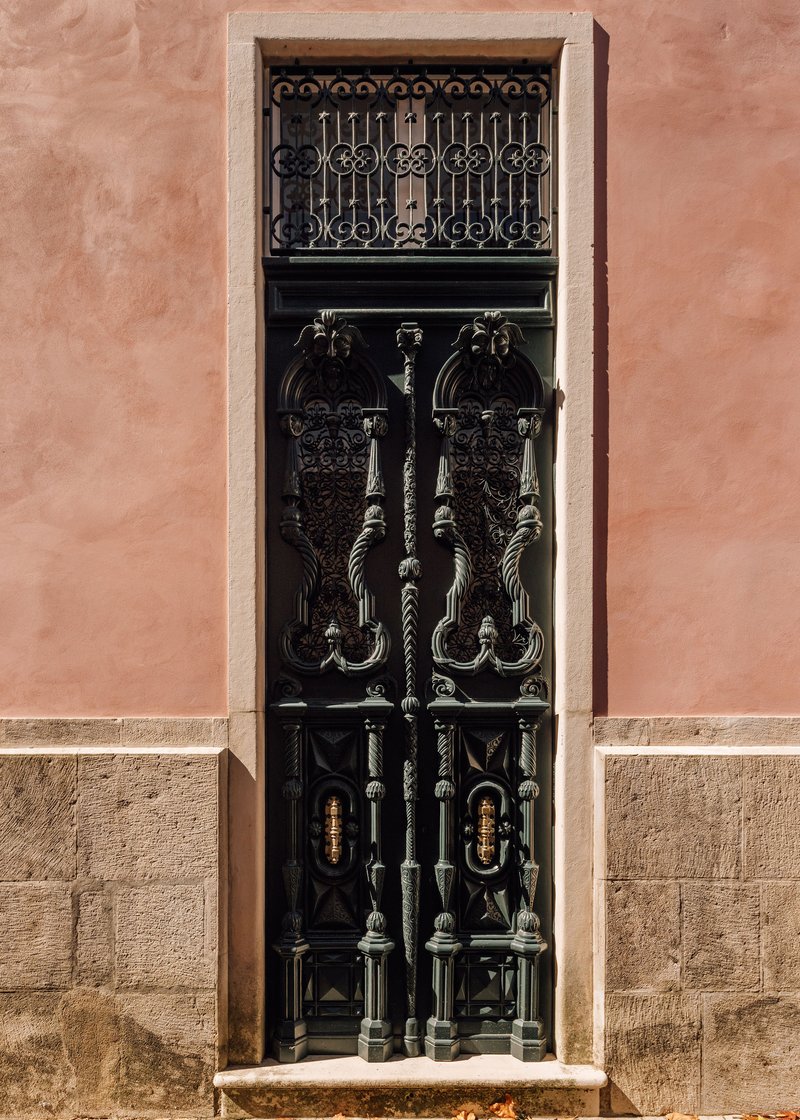Black ornamental metalwork door with transom grille set in a stone and plaster facade