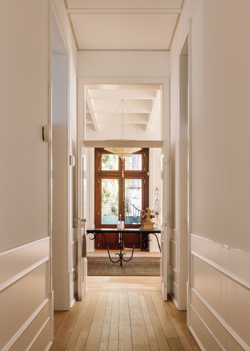 Axial view through white paneled hallway toward timber console table beneath a window with daylight