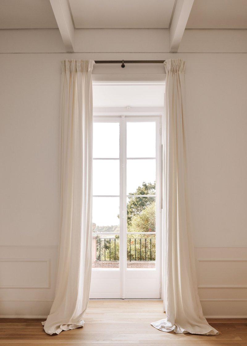 Tall French doors framed by floor-length white curtains opening to a balcony with distant trees