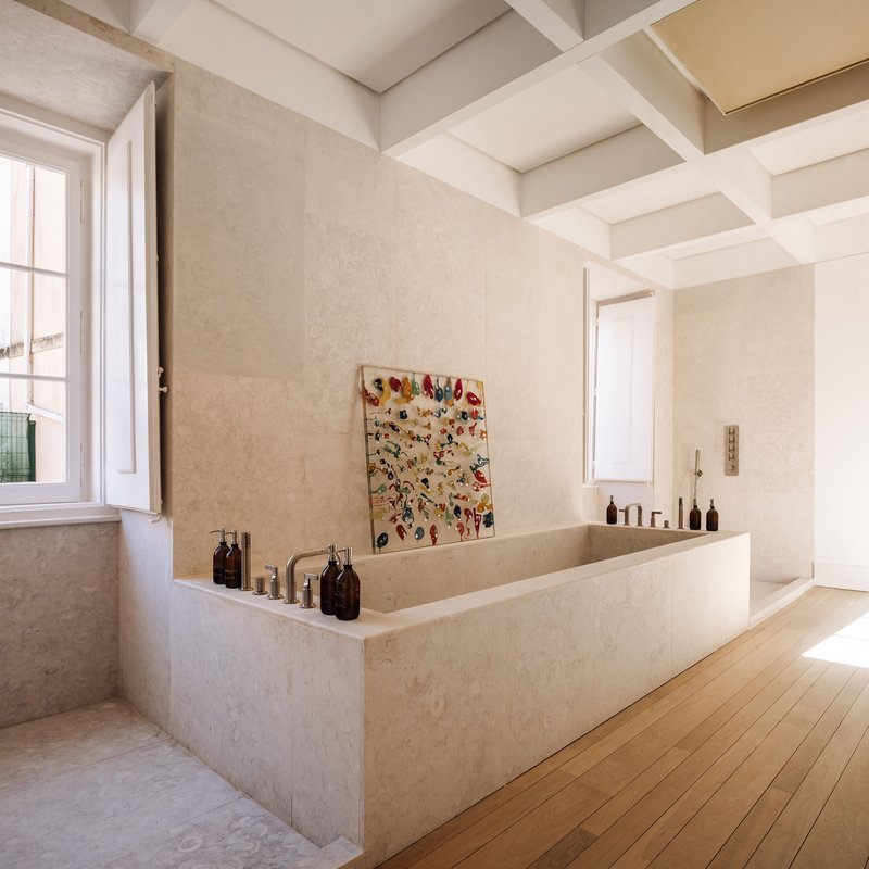 Limestone bathtub surround with coffered ceiling and a painting on the wall beside an open window