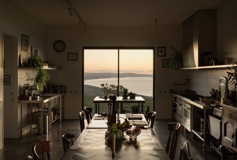 Kitchen with central dining table framing a window view to the sea at dusk