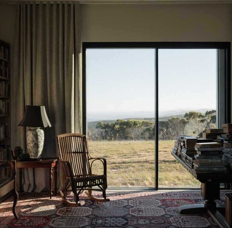 Floor-to-ceiling window framing a view of grassland and distant trees with a rocking chair on a patterned rug