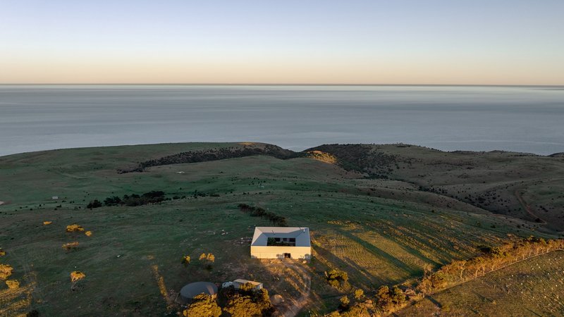 Aerial view of a white rectangular building on sloped farmland overlooking the ocean at dusk
