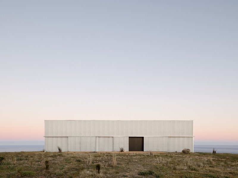 Horizontal corrugated metal facade with central opening set against dry grassland at dusk