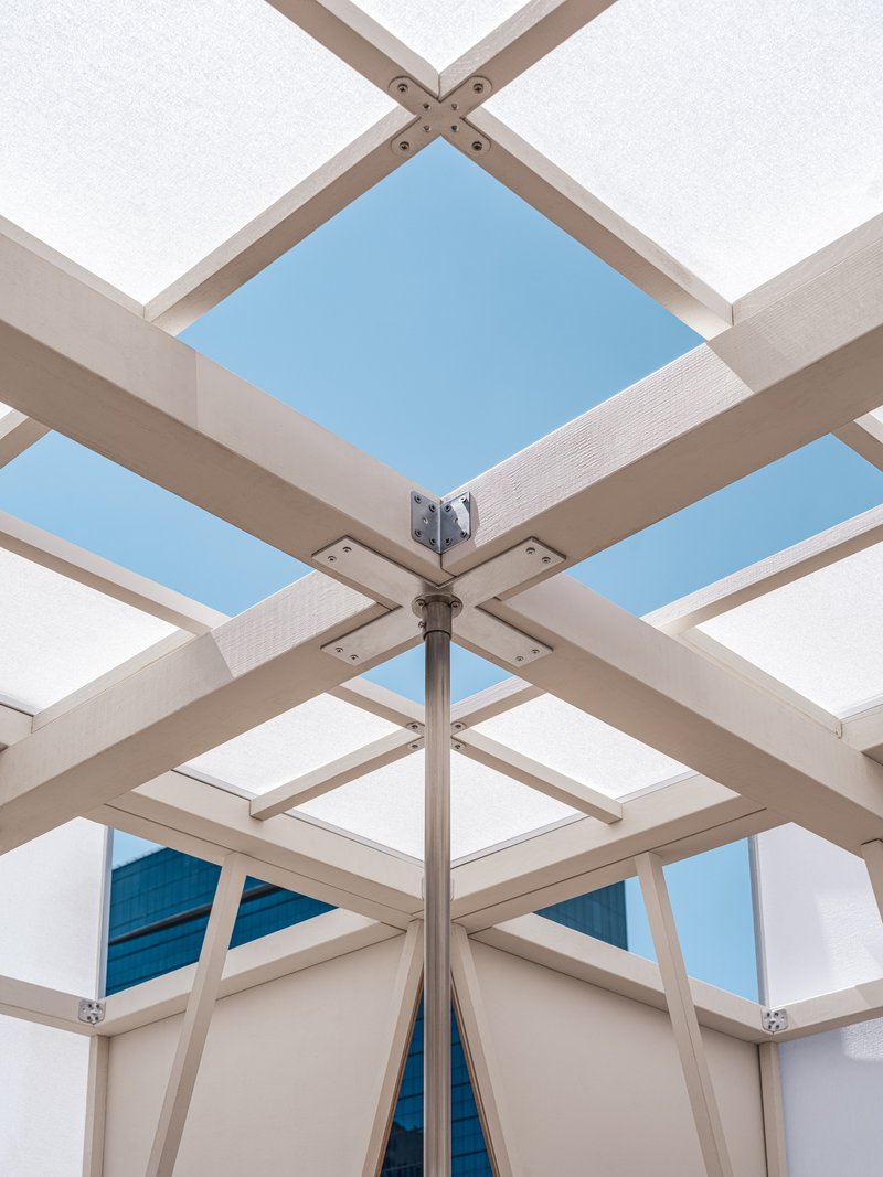 Upward view of the pavilion's central steel column connecting timber beams and translucent roof panels