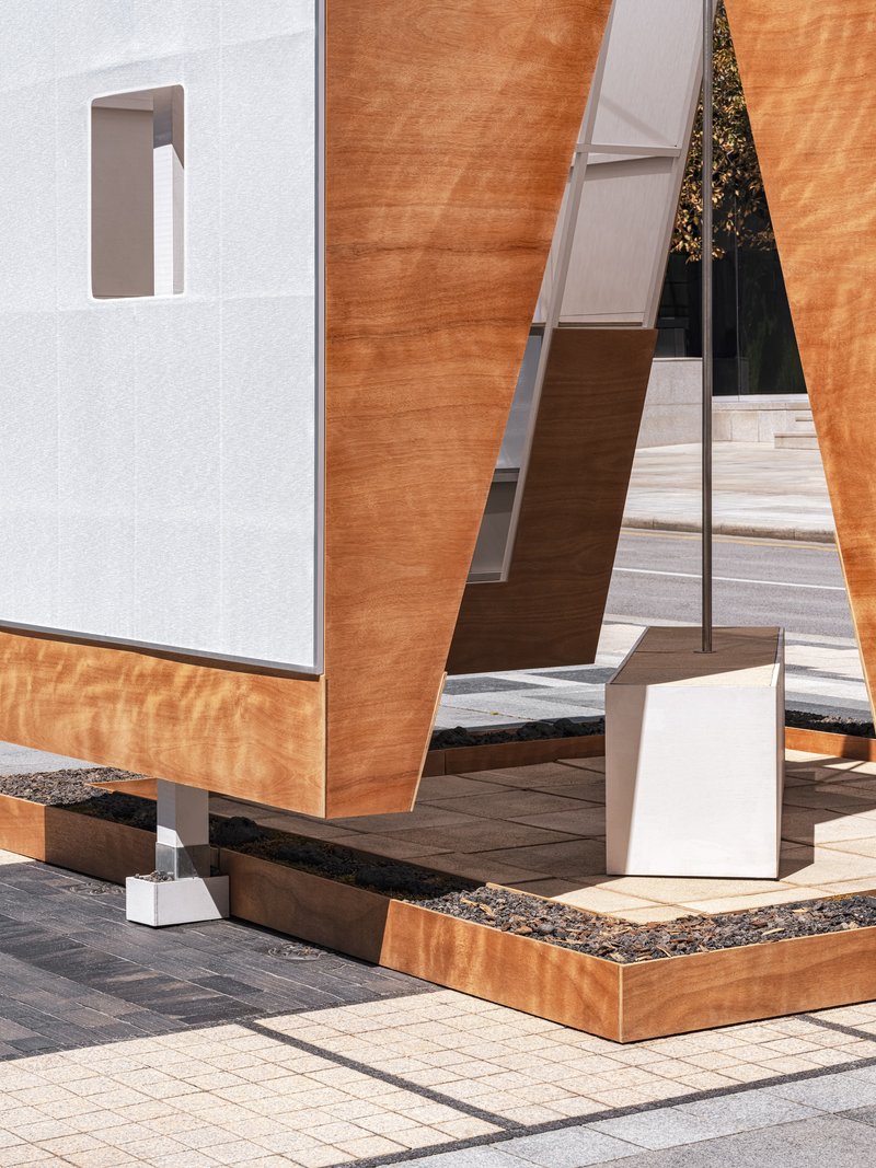 Ground-level detail of laminated timber panels on white metal posts with a black aggregate base