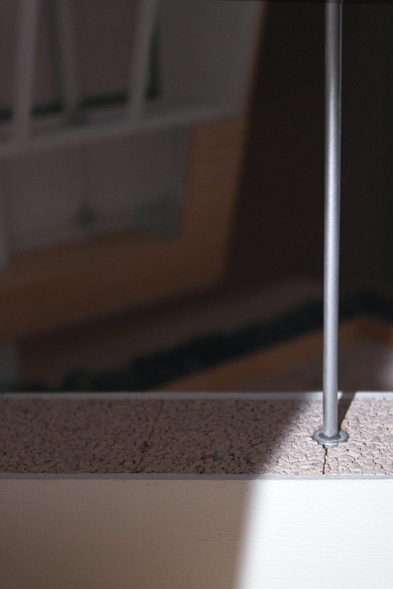 Detail of a slender steel rod anchored into a speckled terrazzo floor