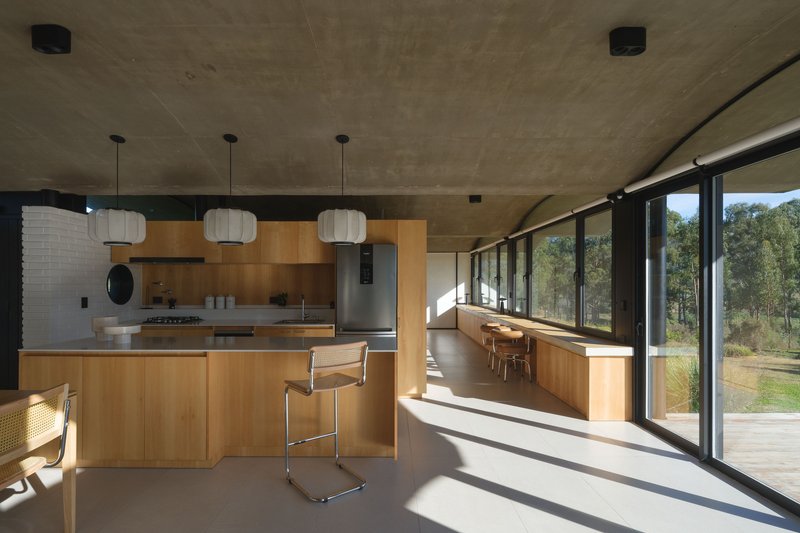 Open-plan kitchen and dining area with exposed concrete ceiling vault and floor-to-ceiling glazing overlooking the landscape