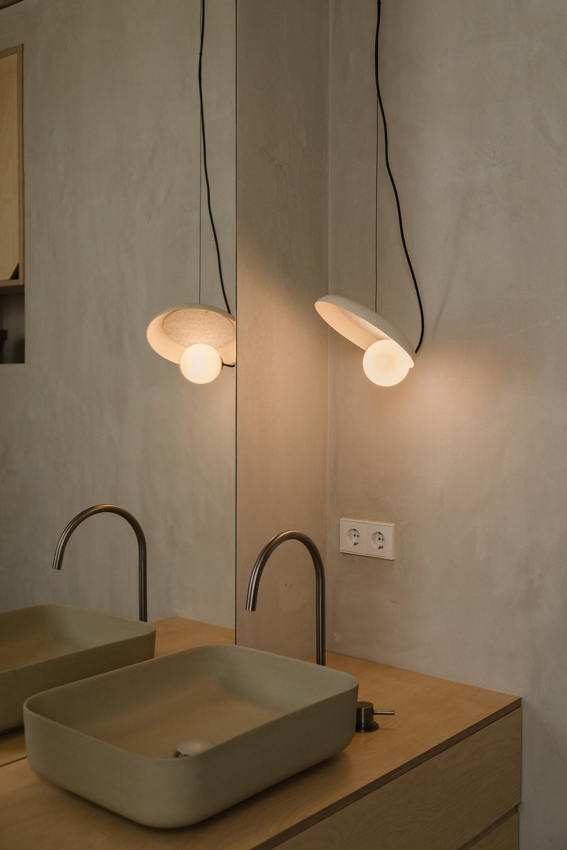 Close-up of the illuminated pendant lights suspended above pale green vessel sinks with arched faucets